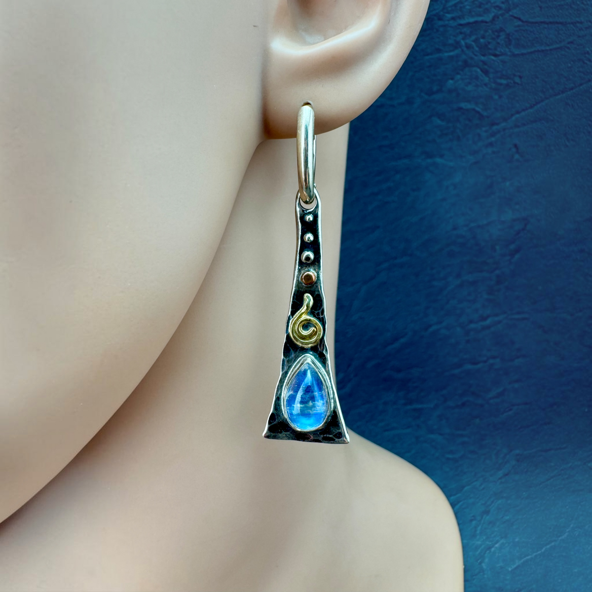 Rainbow Moonstone Triangle Flair Earring shown on the ear, hammered sterling silver with 18k gold spiral